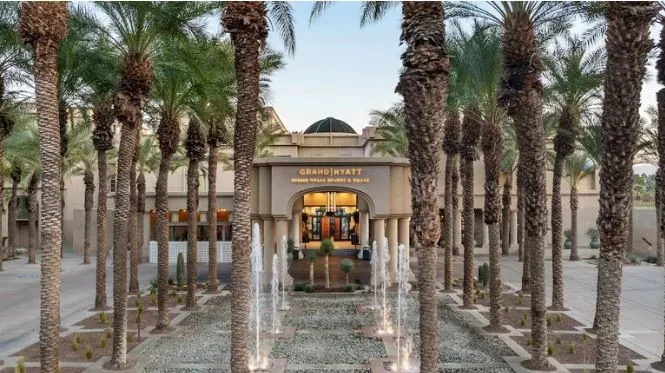 The entrance of the Grand Hyatt Indian Wells, showcasing its lush composition of palm trees and water jet fountains.